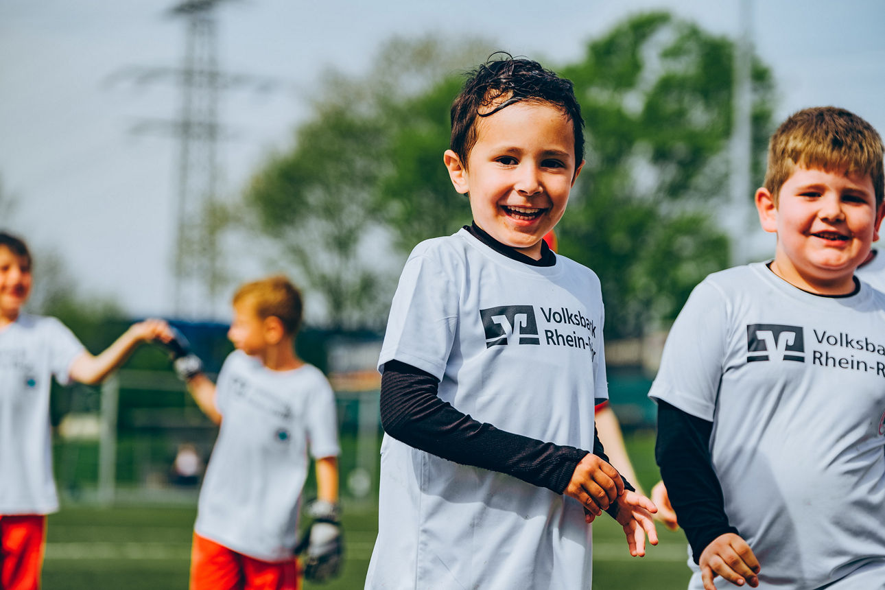 Eine Kinder-Fußballmannschaft in Volksbank-Trikots feiert einen Torschützen