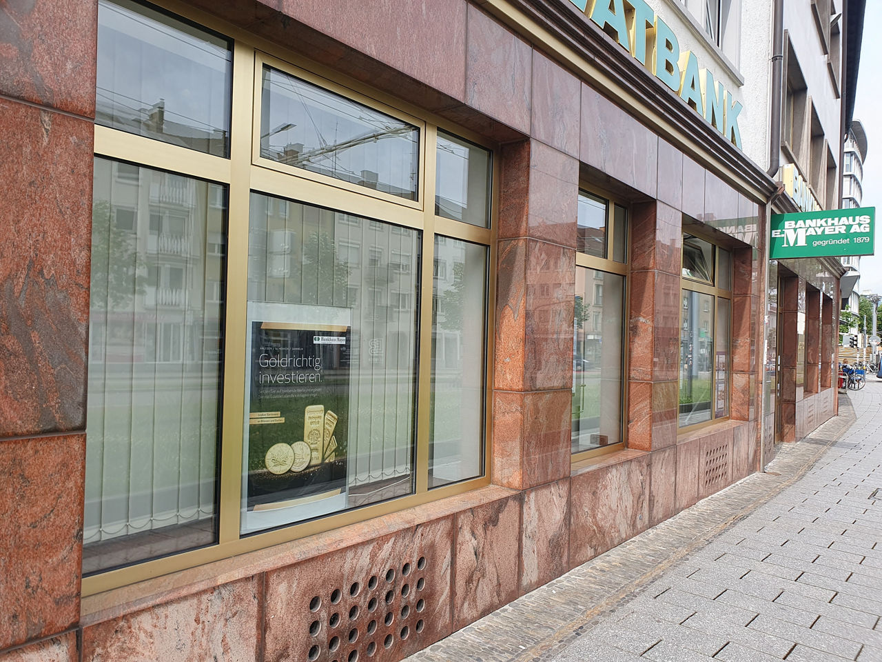 Eine Reihe großer Schaufenster mit goldfarbenen Rahmen in einer braun verkleideten Gebäudefassade Tische und Stühle