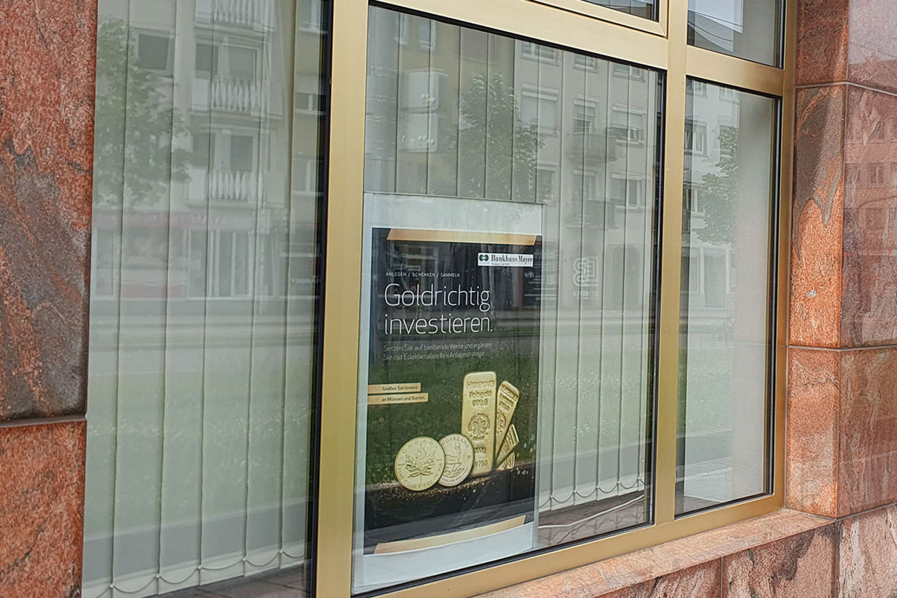 Eine Reihe großer Schaufenster mit goldfarbenen Rahmen in einer braun verkleideten Gebäudefassade