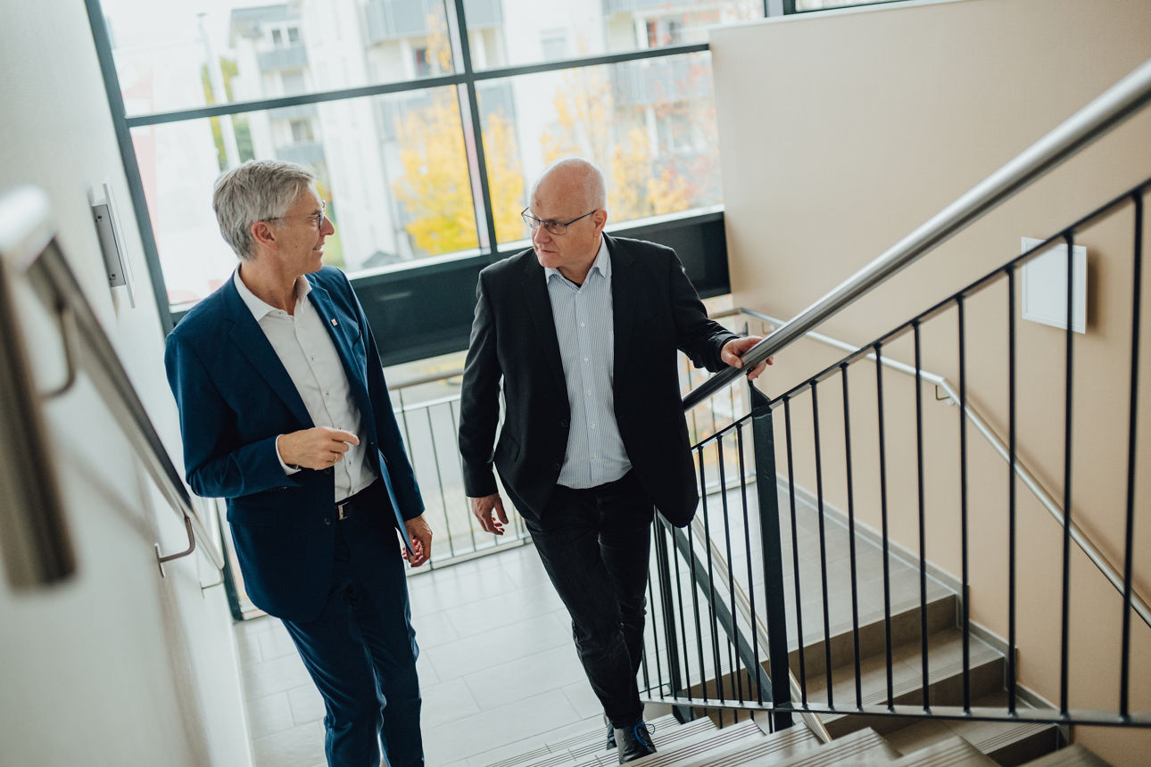 Zwei Mitarbeitende unterhalten sich und gehen eine Treppe hoch