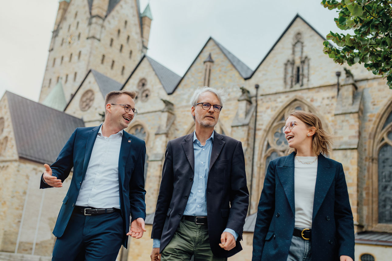 Drei Mitarbeitende stehen vor dem Paderborner Dom