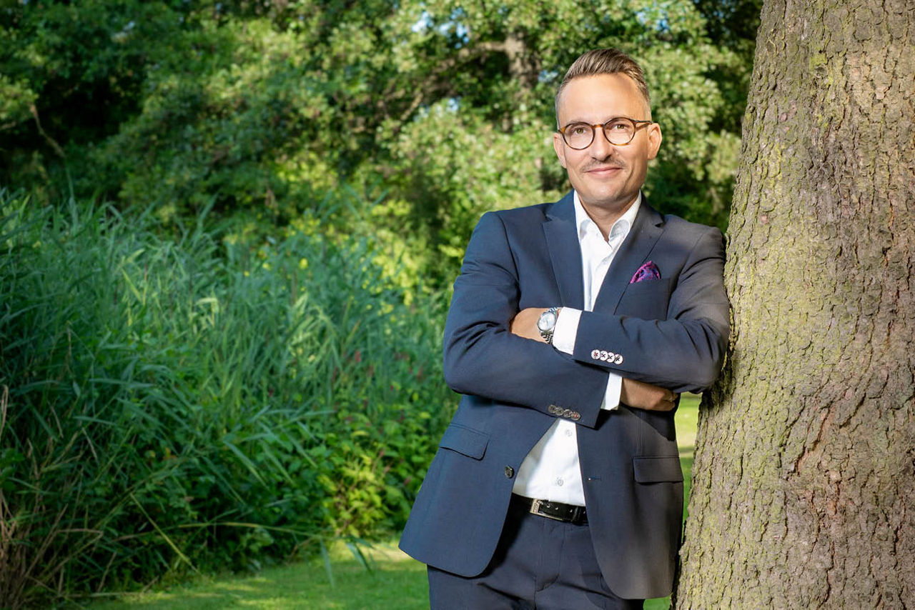 Mann lehnt mit verschrenkten Armen am Baum