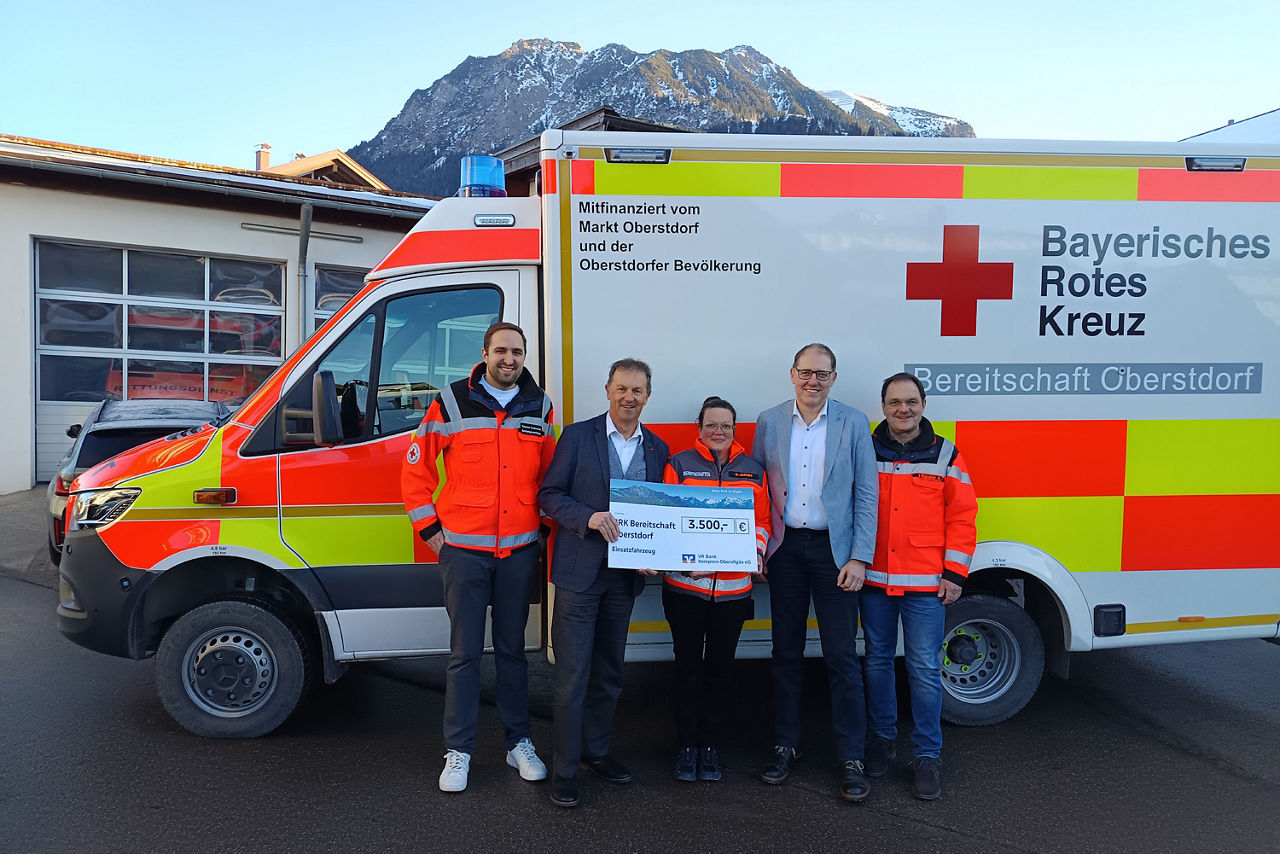 BRK-Bereitschaft Oberstdorf neues Einsatzfahrzeug - Bild der Spendenübergabe - 5 Personen stehen vor einem Rettungswagen und halten einen Spendenscheck
