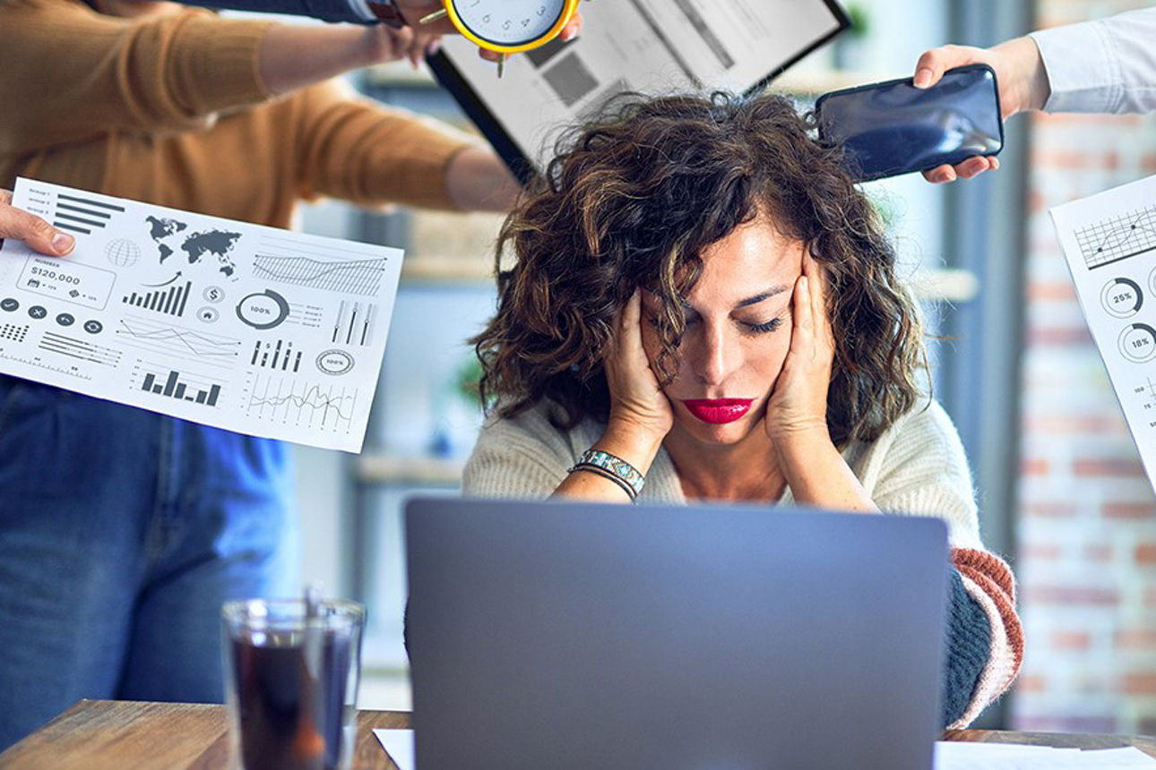 Eine Frau sitzt  psychisch erschöpft über ihrem Schreibtisch.