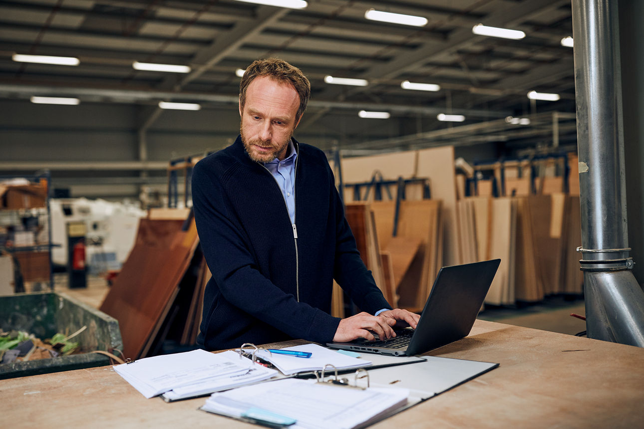 Mann steht in Werkstatt vor einem Tisch an seinem Notebook