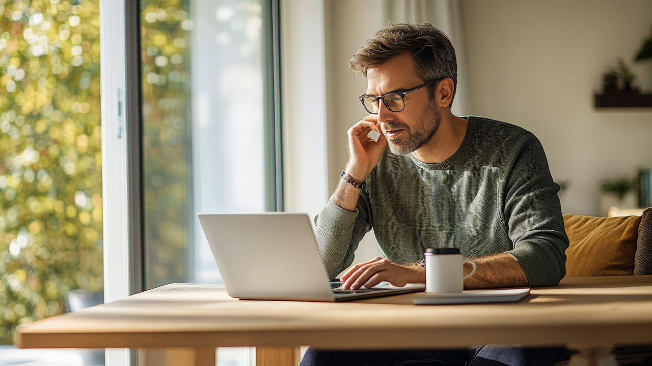Mann am Esstisch schaut in sein Laptop