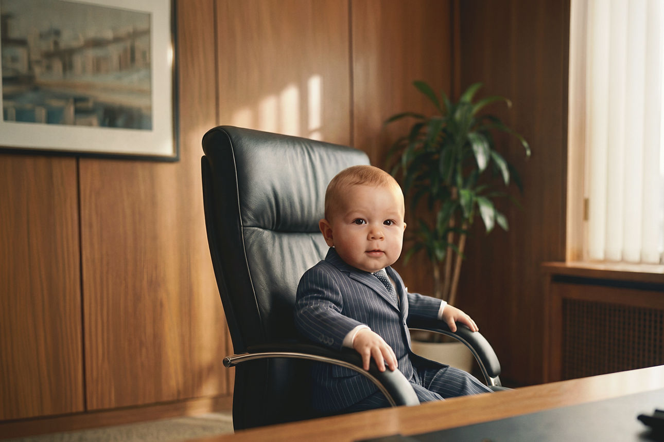 Baby sitzt im Anzug auf dem Bürostuhl.