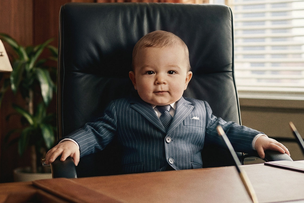 Ein Baby sitzt im Bürostuhl am Schreibtisch.