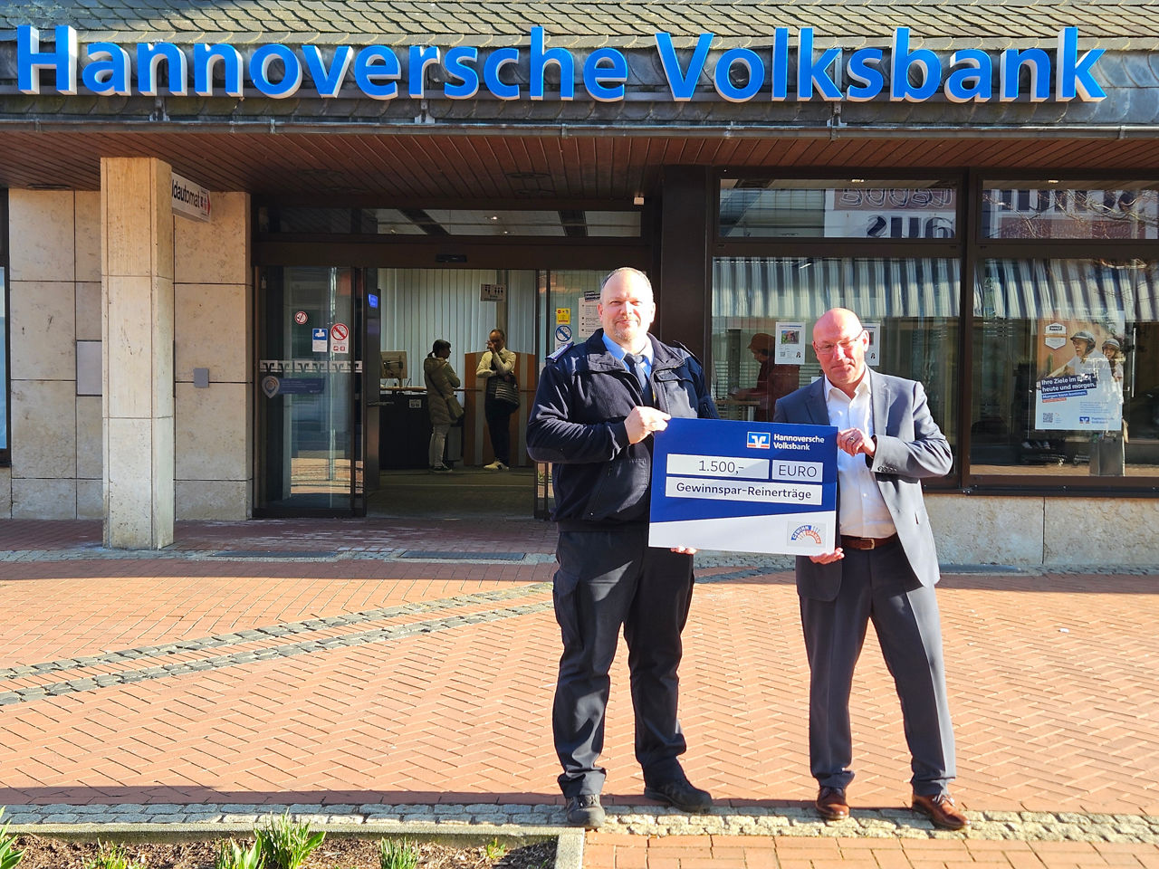 Zwei Personen halten ein Schild in der Hand, auf dem 1.500 EURO Gewinnspar- Reinerträge steht