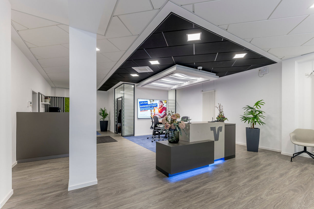 Moderner Empfangsbereich mit Empfangstresen, zwei Pflanzen und Stuhl vor weißer Wand mit Heizkörper