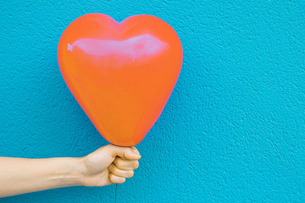 Luftballon in Herzform wird in einer Hand festgehalten