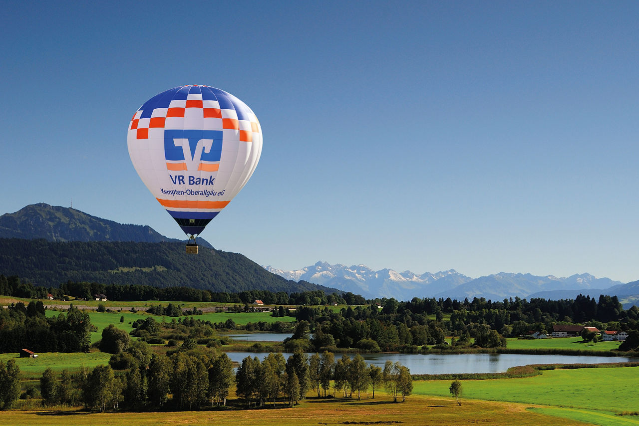 VR Bank Heißluftballon schwebt über dem Niedersonthofener See - im Hintergrund sieht man Grünten und die Allgäuer Berge