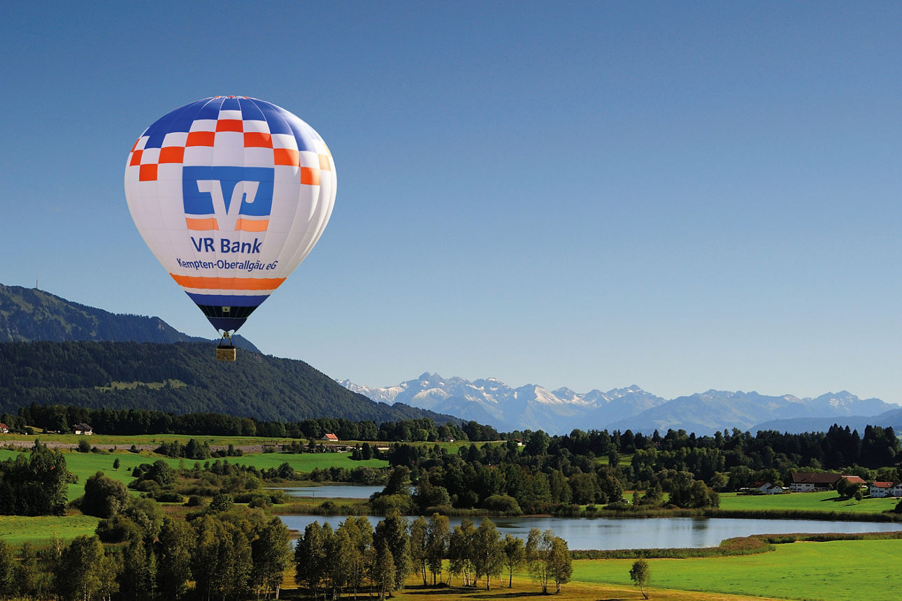 Blick auf den Niedersonthofener See mit Ballon der VR Bank - im Hintergrund sind der Grünten und die Allgäuer Berge zu sehen