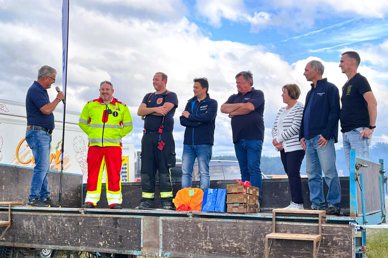 Zwei Vorstände mit den Helfern auf einer Bühne im Freien.