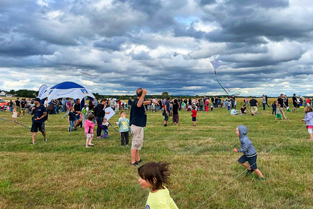 Eine Wiese mit vielen Erwachsenen und Kindern, die Drachen steigen lassen.