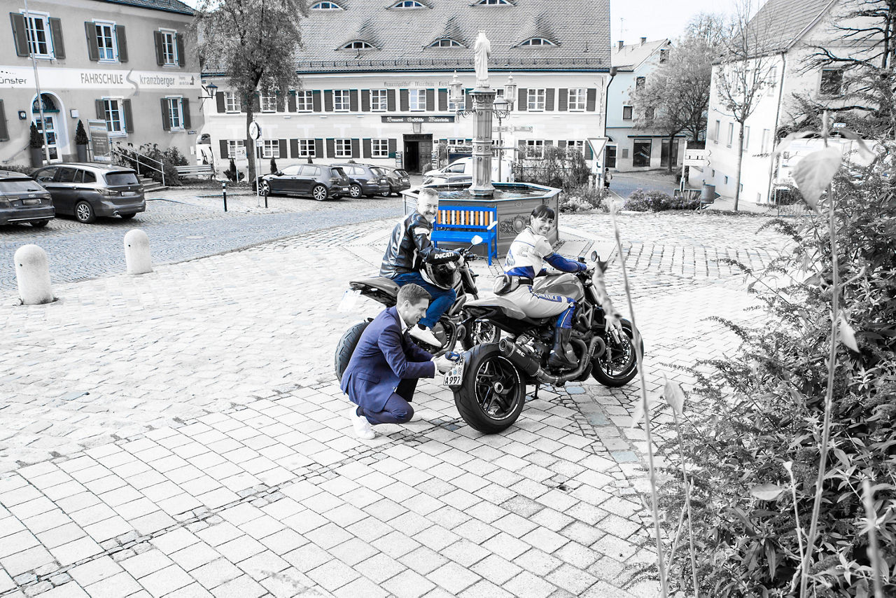 Eine Frau und zwei Männer befinden sich mit zwei Motorrädern auf einem Marktplatz