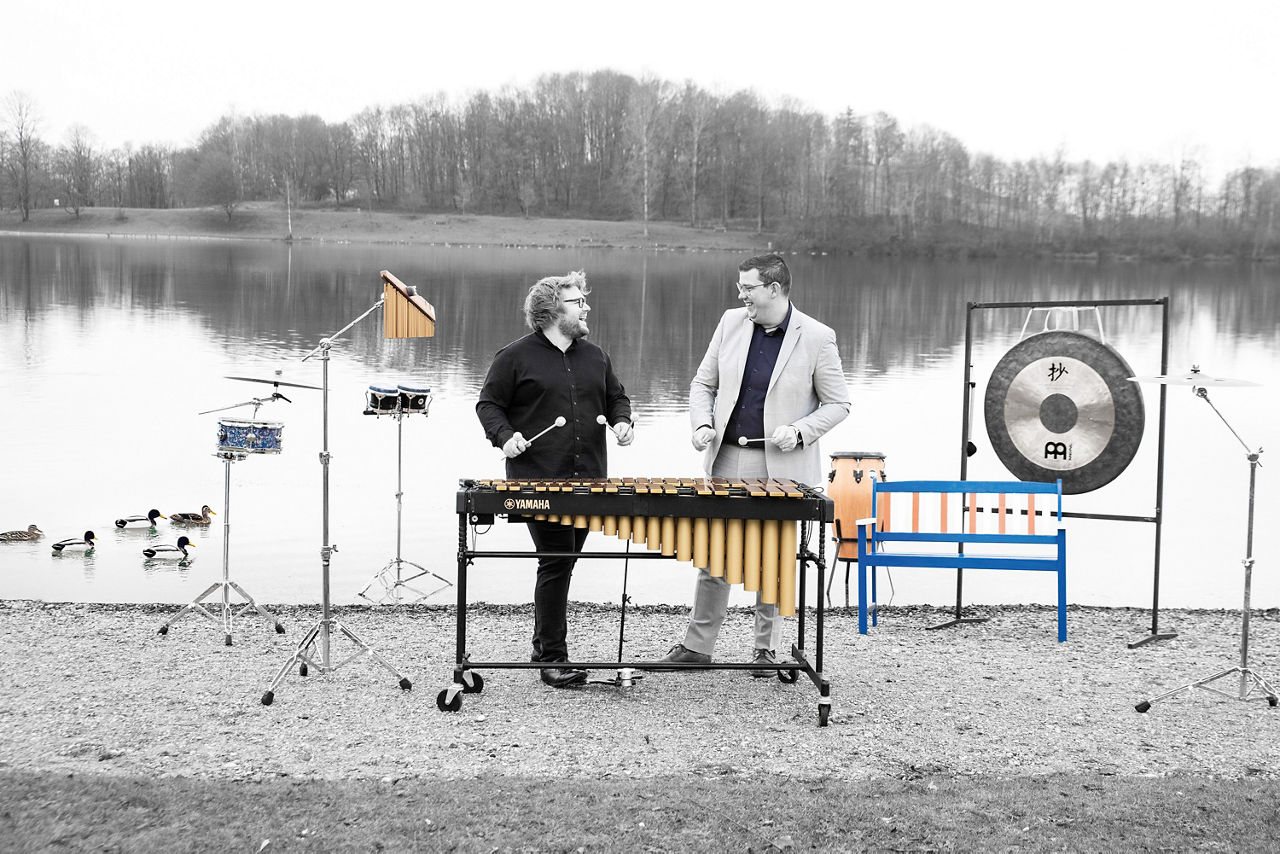 Zwei Männer stehen mit Musikinstrumenten am Ufer eines Sees