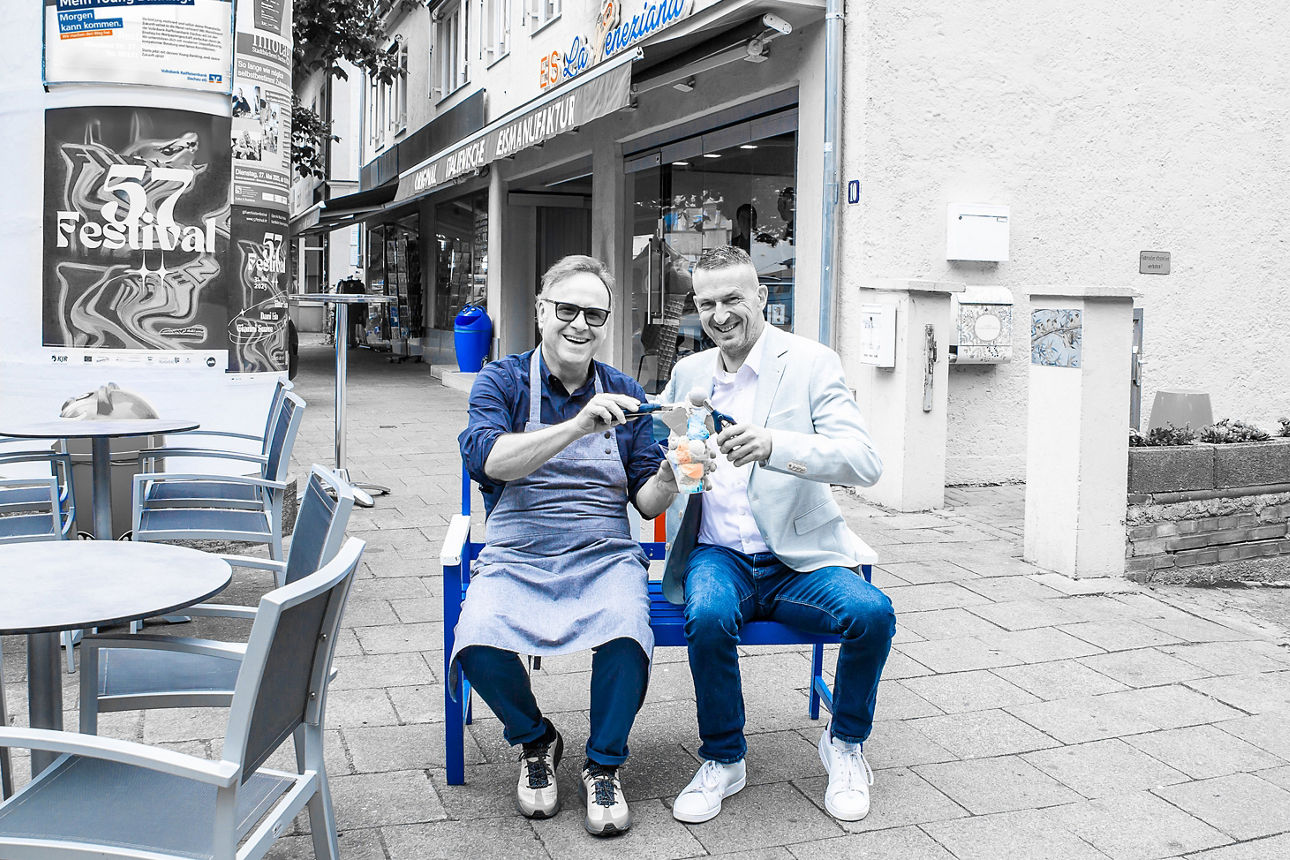 Zwei Männer sitzen auf einer Bank mit einem Eis in der Hand sitzen vor einer Eisdiele