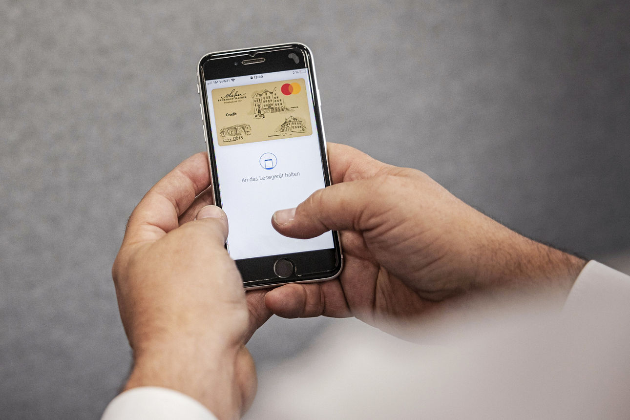 Ein Mann hält ein Handy in der Hand, auf dem eine goldene Kreditkarte zu sehen ist.