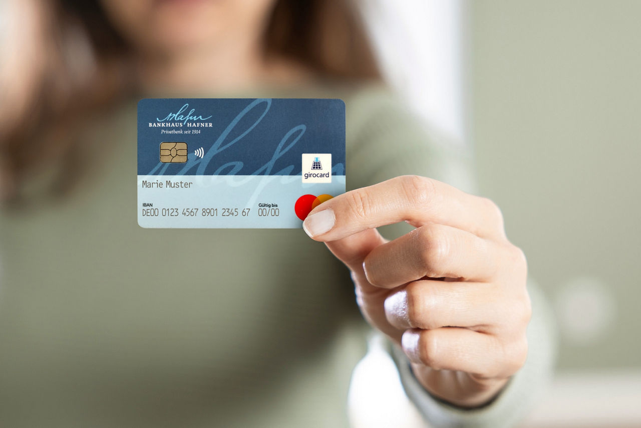 Eine Frau hält eine blaue girocard mit dem Logo des Bankhaus Hafner in die Kamera.