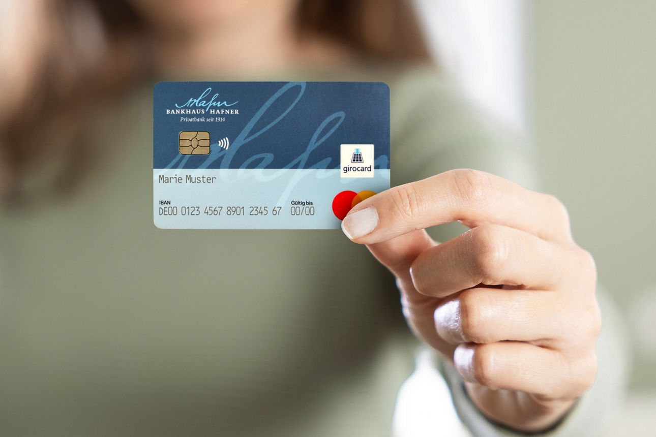 Eine Frau hält eine blaue girocard mit dem Logo des Bankhaus Hafner in die Kamera.