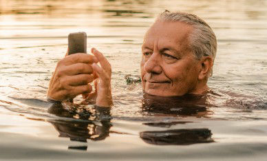 Mann im Gras lächelt in sein Handy