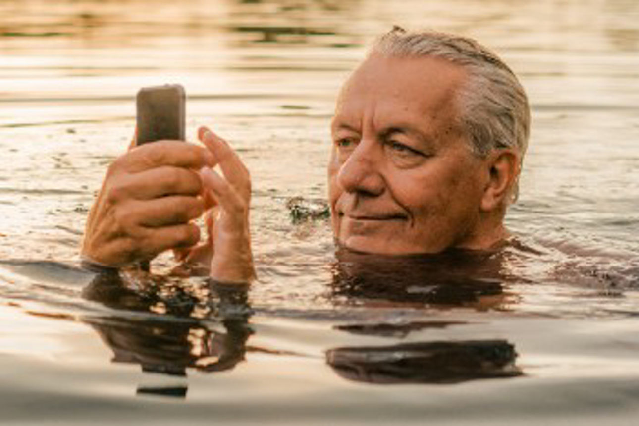 Mann im Gras lächelt in sein Handy