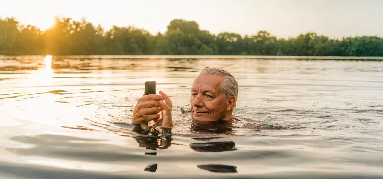 Mann liegt lächelnd im Gras und schaut auf sein Mobiltelefon
