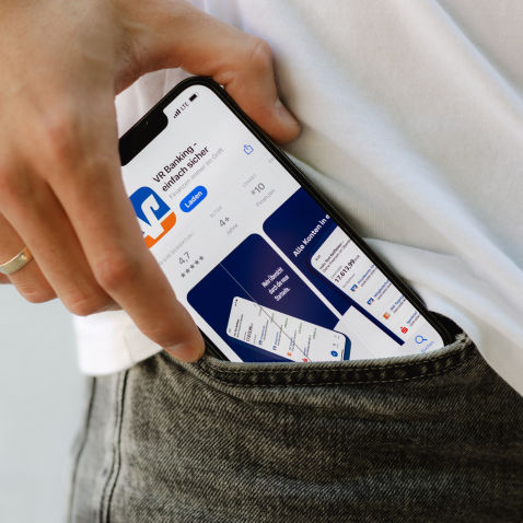 Eine Person zieht ein Smartphone mit der VR Banking App aus der Hosentasche.