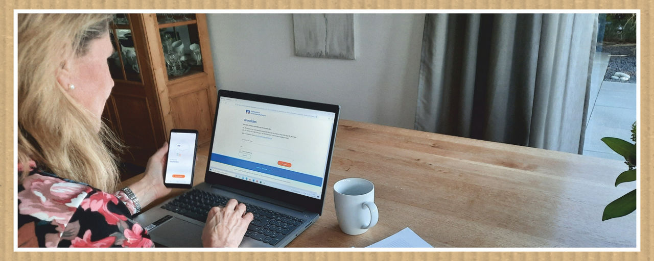 Eine Frau sitzt mit dem Handy vor dem Laptop