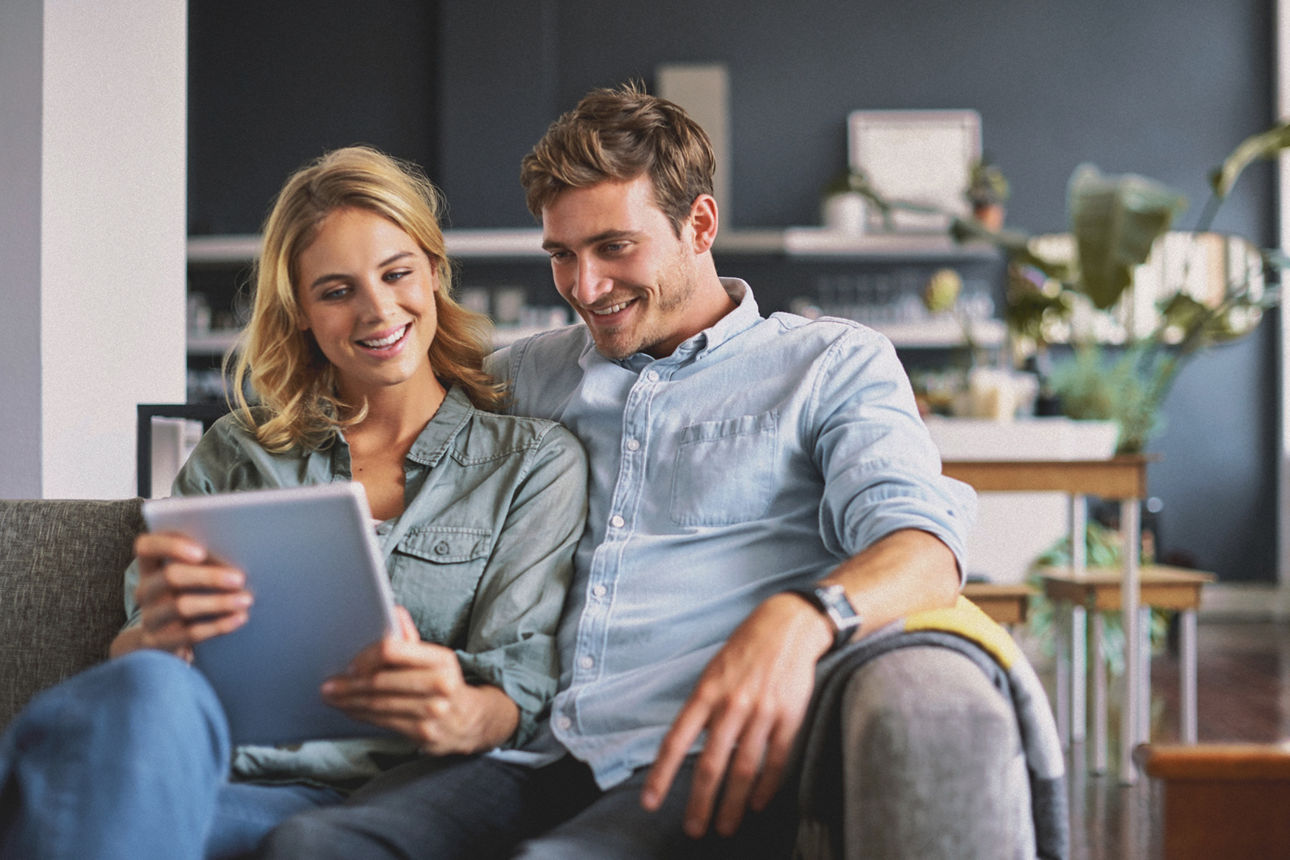 Zwei Personen sitzen entspannt zusammen und schauen lächelnd auf ein Tablet.