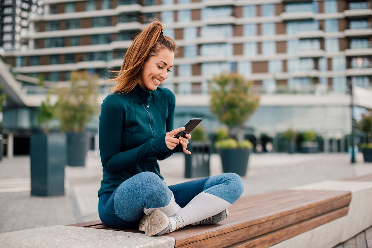 Frau sitzt auf einer Bank in der Stadt und schaut auf ihr Smartphone