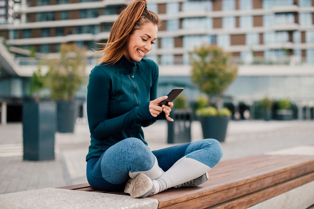 Frau sitzt auf einer Bank in der Stadt und schaut auf ihr Smartphone