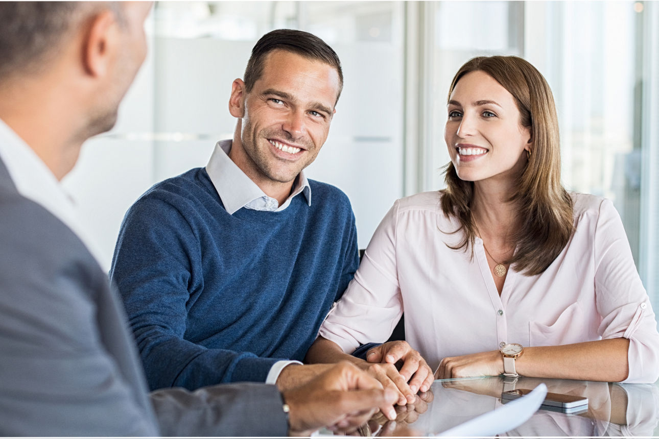 Drei Personen sitzen an einem Tisch in einem hellen Büro und sprechen miteinander.