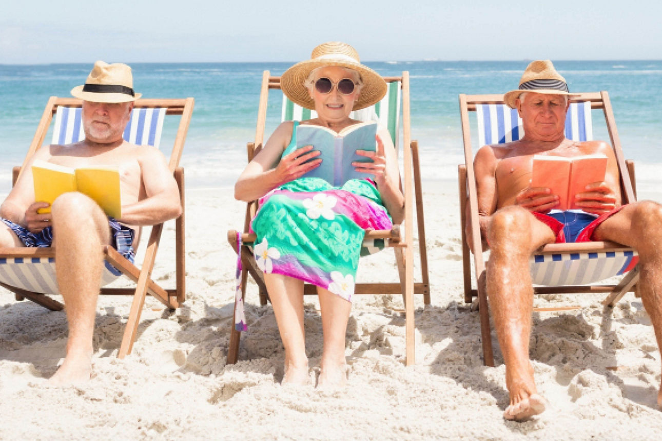 Vier ältere Menschen lesen gemeinsam in einem Strandkorb am Strand.