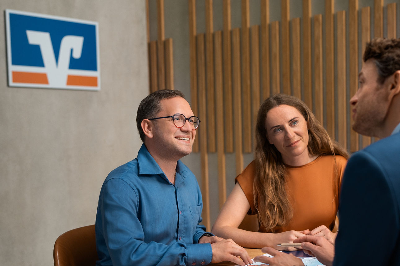 Zwei Männer und eine Frau sitzen an einem Tisch und führen ein Gespräch