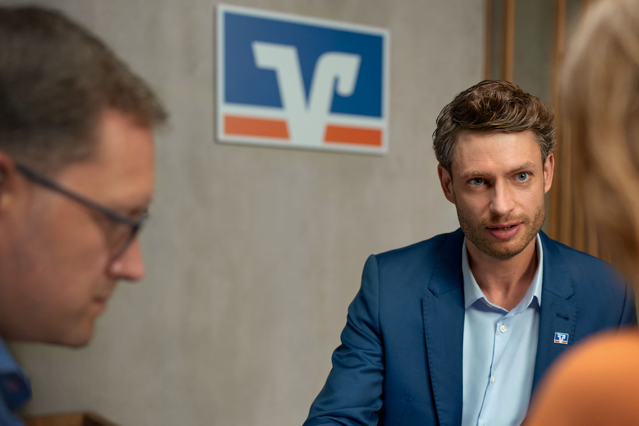 Zwei Männer und eine Frau sitzen an einem Tisch und führen ein Gespräch