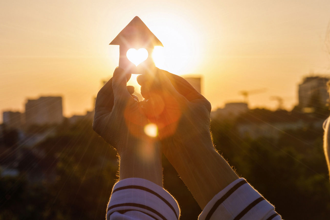 Eine Person hält eine Hausfigur in das Licht der Sonne.