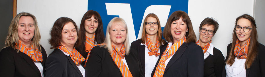 acht Frauen stehen in einer Reihe vor einer Mauer