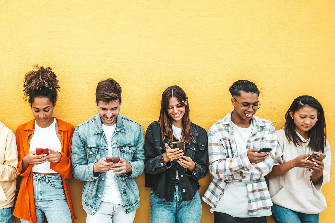 Mehrere Personen stehen vor einer gelben Wand und überprüfen ihre Smartphones.