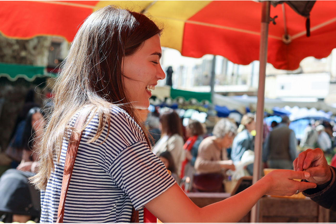 Frau kauft auf belebtem Markt an einem sonnigem Tag ein.