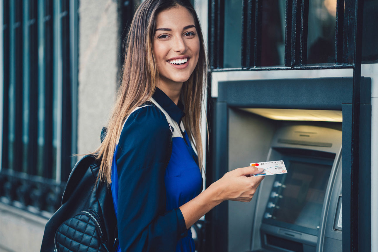Eine Frau steht mit der girocard vor einem Geldautomaten