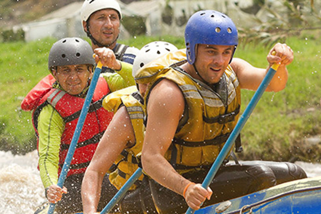 Eine Gruppe von Menschen in bunten Flößen fährt auf einem Fluss, umgeben von üppigem Grün und blauem Himmel. 