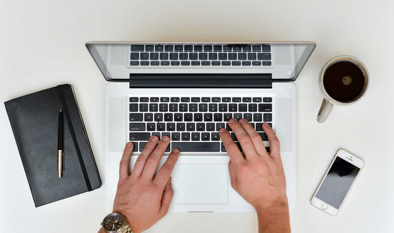 Basiskonto - Hände tippen auf Laptop Handy und Kaffe stehen rechts