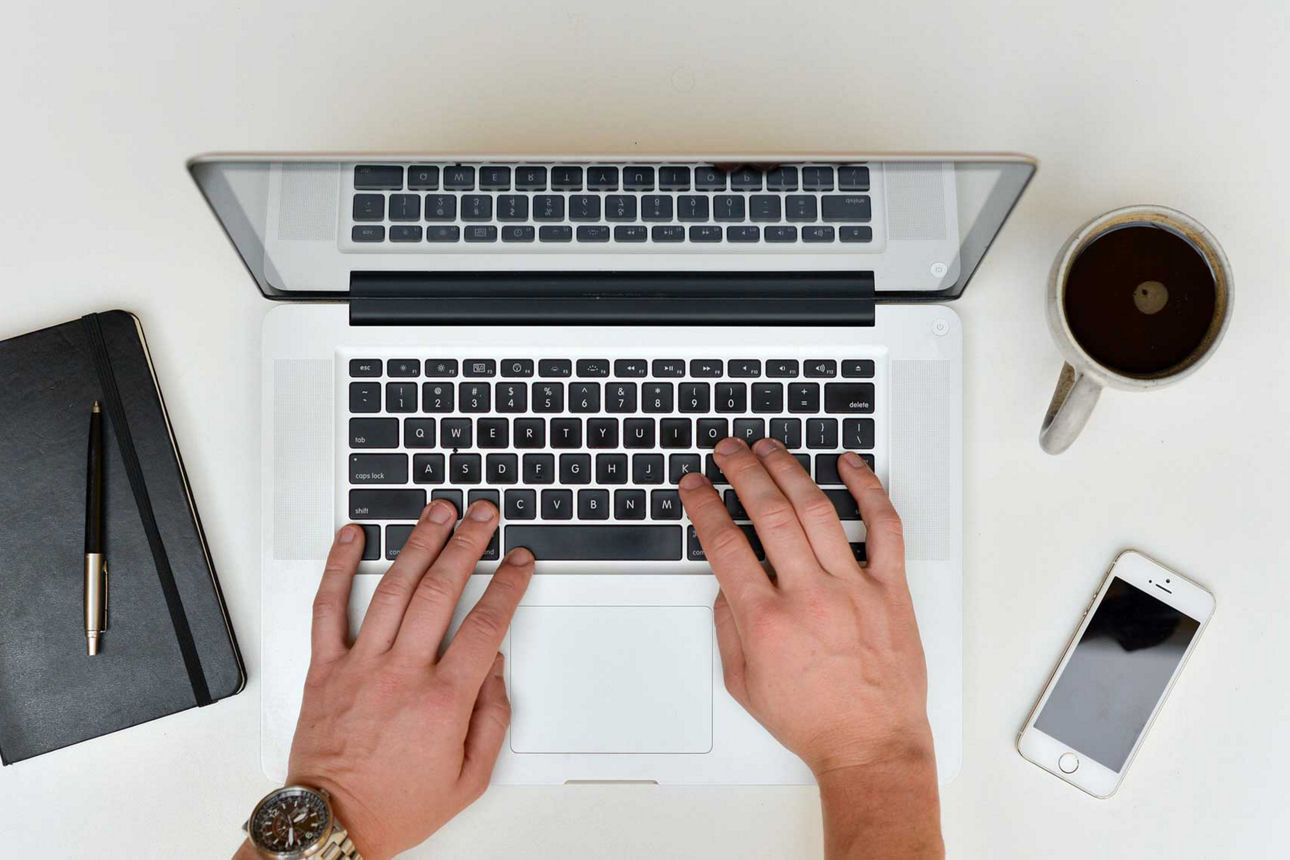 Basiskonto - Hände tippen auf Laptop Handy und Kaffe stehen rechts