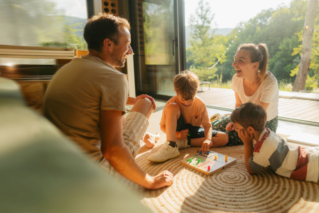 Familie mit Bauhelmen steht von einem Rohbau, der Mann hält einen Bauplan in der Hand