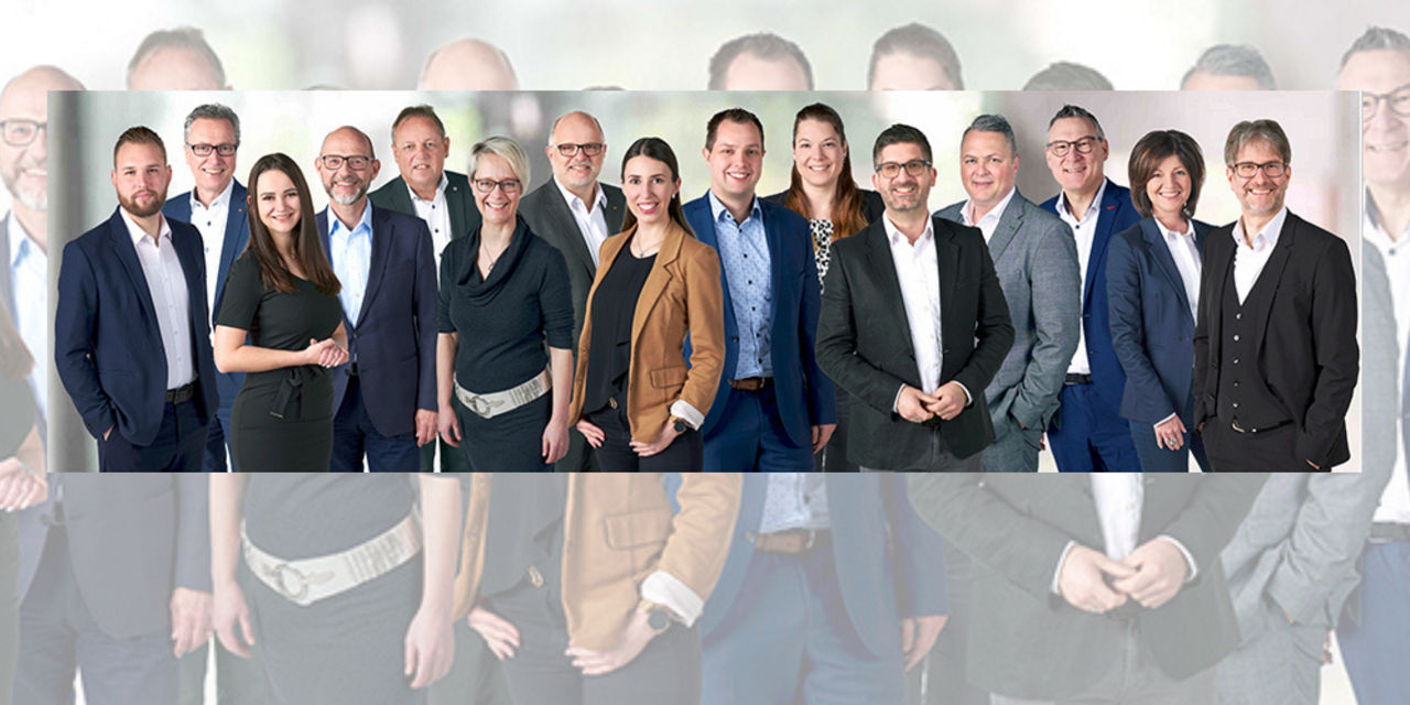 Eine Gruppe von Personen in formeller Kleidung steht zusammen vor einem neutralen Hintergrund.