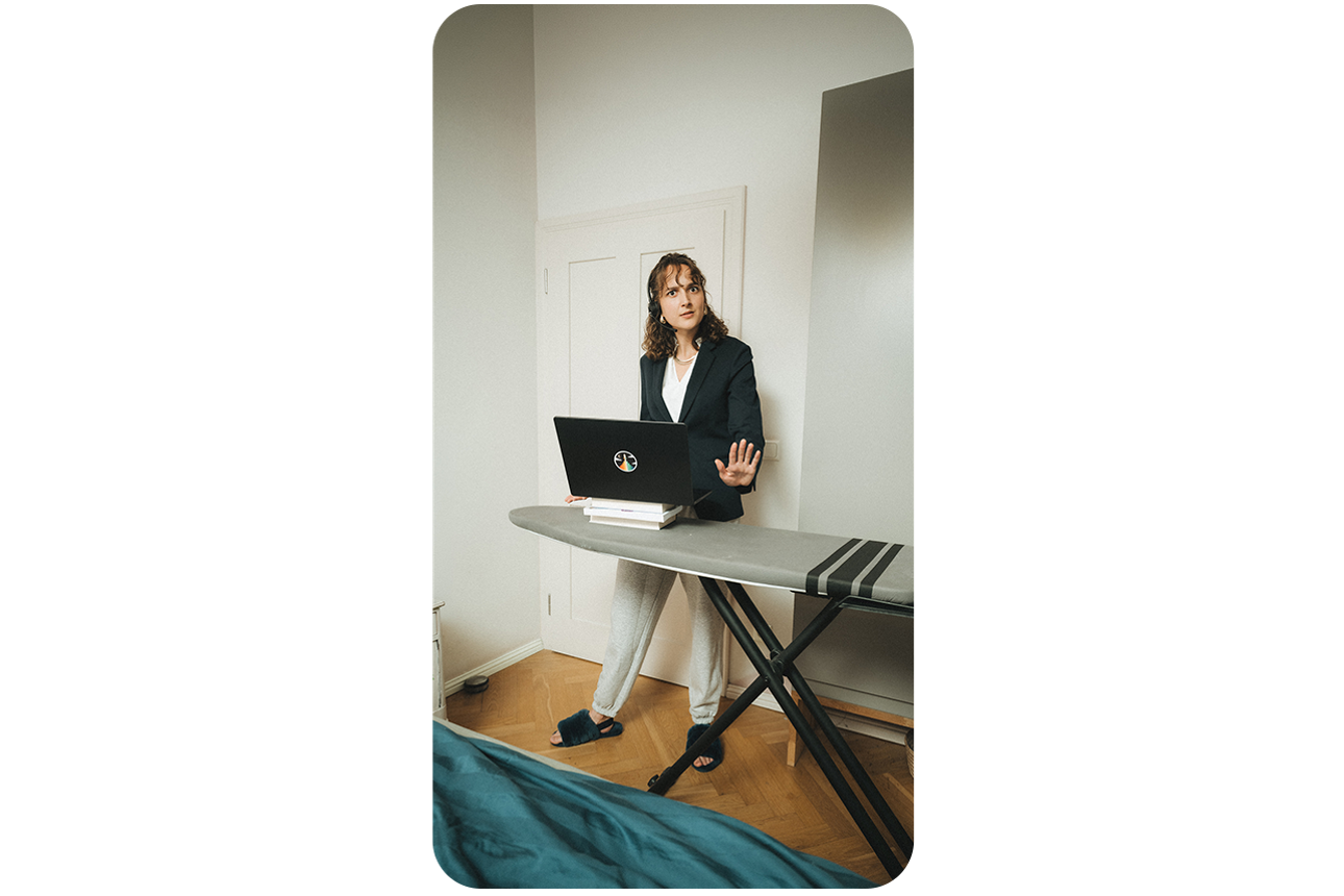 Frau steht an einem Bügelbrett mit Ihrem Laptop und hat ein Business Gespräch.