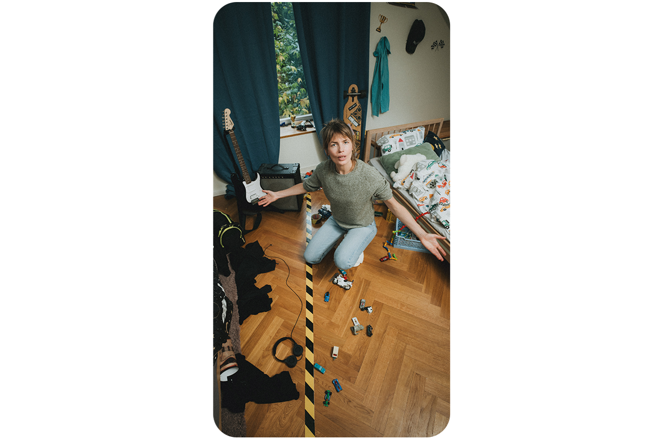 Frau hockt auf dem Boden eines Kinderzimmers, welches durch eine Trennlinie in 2 geteilt wurde.