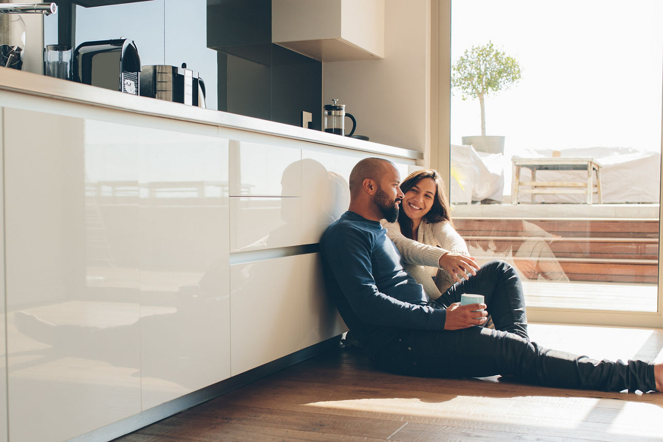 Paar sitzt in der Küche auf dem Boden und trinkt Kaffee
